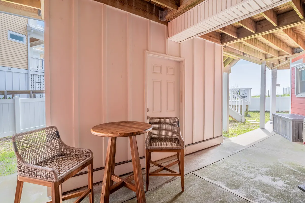 A wooden table and two chairs are arranged near a doorway, suggesting an inviting spot to relax, socialize, or enjoy drinks. The setting is casual and could easily represent a porch or deck where guests gather for cocktails before heading out to explore local hotspots. Natural light enhances the welcoming atmosphere.