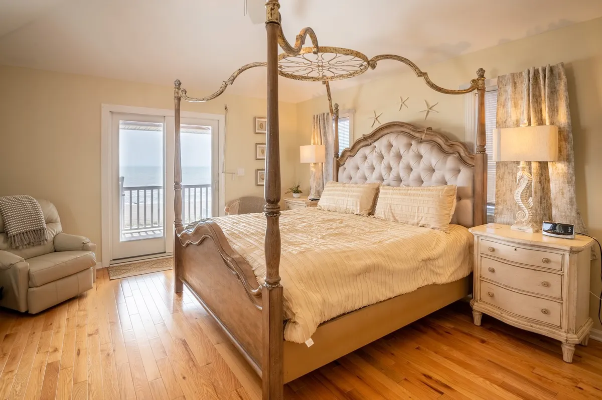 A serene bedroom featuring a canopy bed positioned to take advantage of an expansive ocean view through large windows. The room also includes a nightstand with a lamp and an armchair, offering a peaceful space to relax and enjoy the scenery.