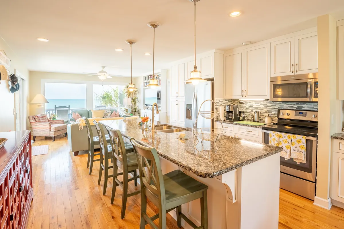 A welcoming interior showcasing a modern kitchen with a central island, stylish light fixtures, and a dining table set for a group. The ocean is visible through the windows, highlighting the seamless flow between dining, cooking, and the natural surroundings.