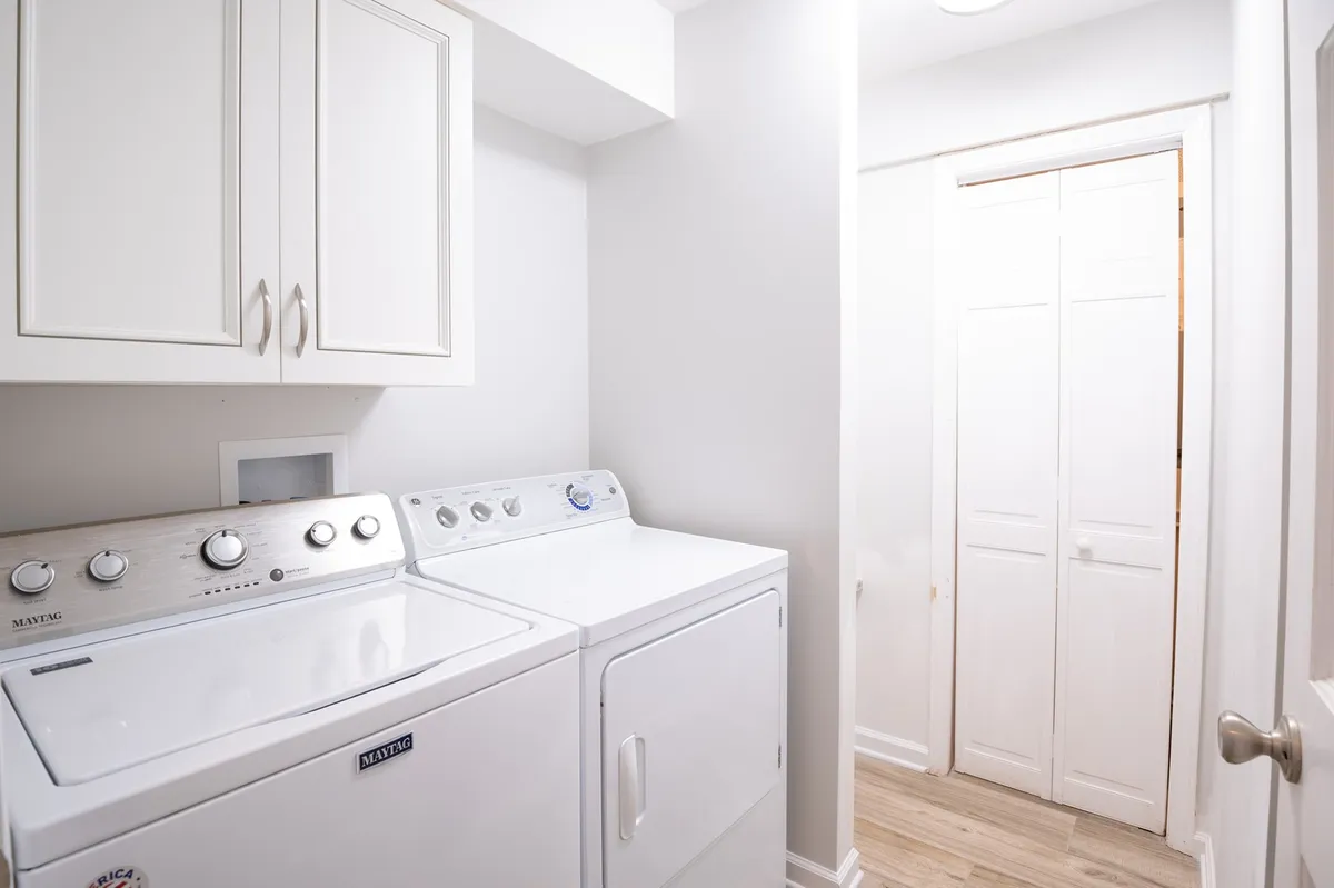A well-lit, practical laundry room featuring a washing machine and dryer, with cabinets above for storing laundry and cleaning supplies. The space is clean and organized, with a straightforward layout ideal for handling daily chores with ease.
