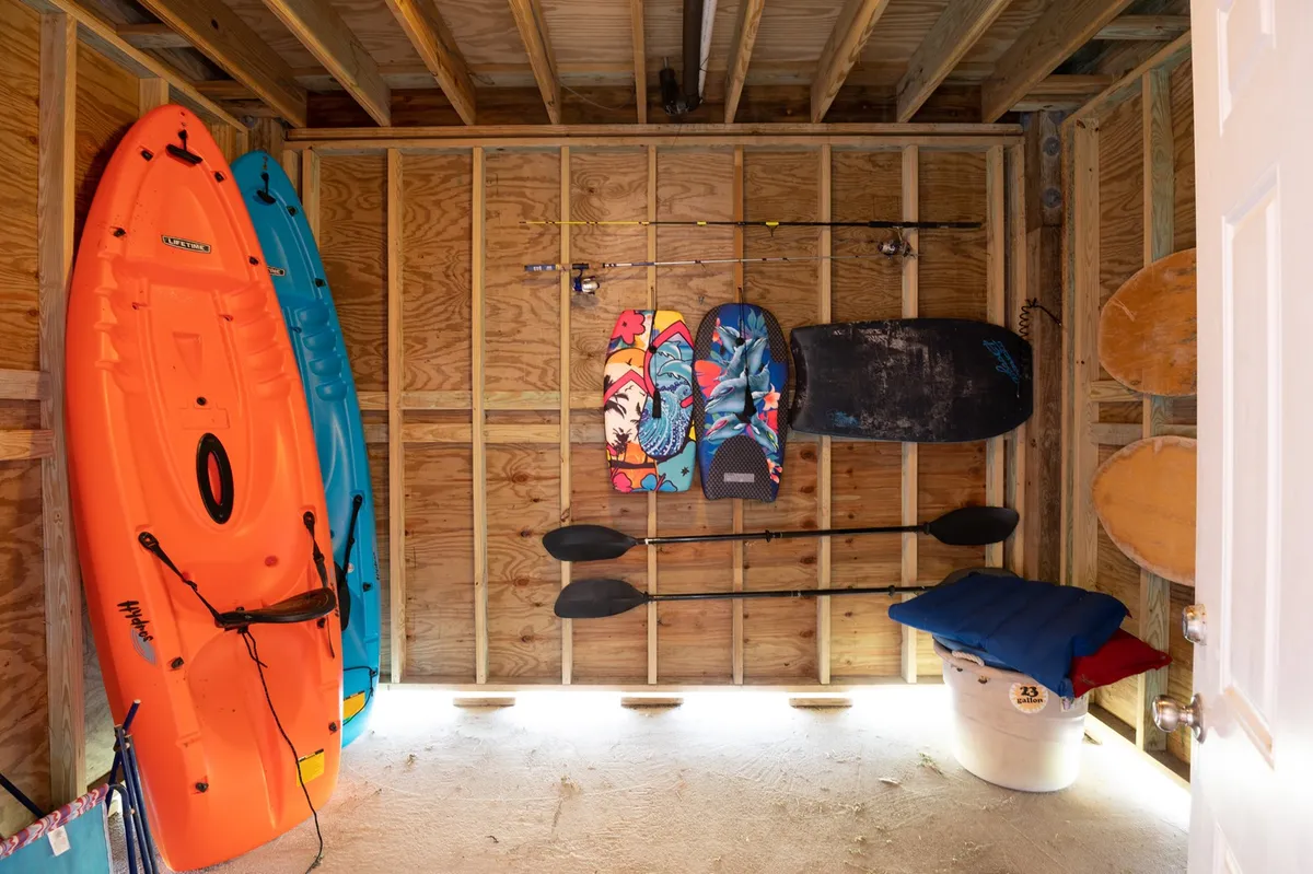 A vibrant storage area filled with kayaks, colorful bodyboards, and fishing rods. The scene hints at the variety of beach equipment available for adventurous guests, ready for coastal escapades.